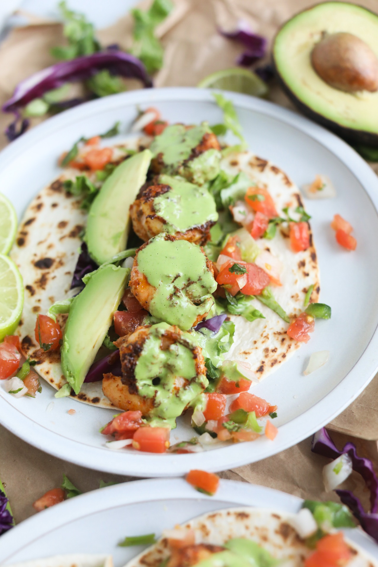 Taco plated on a gray matte plate with blackened shrimp, avocado slices, lettuce, cabbage, pico de gallo with cilantro lime sauce drizzled.