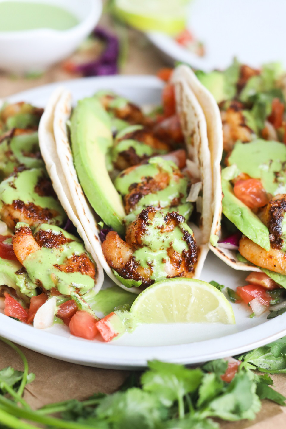 Blackened shrimp tacos with avocado, sliced limes, pico de gallo, lettuce and green sauce drizzle. Slice limes and cilantro added for styling purposes.