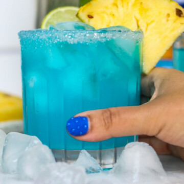 Hand with blue nail on thumb holding blue margarita recipe.