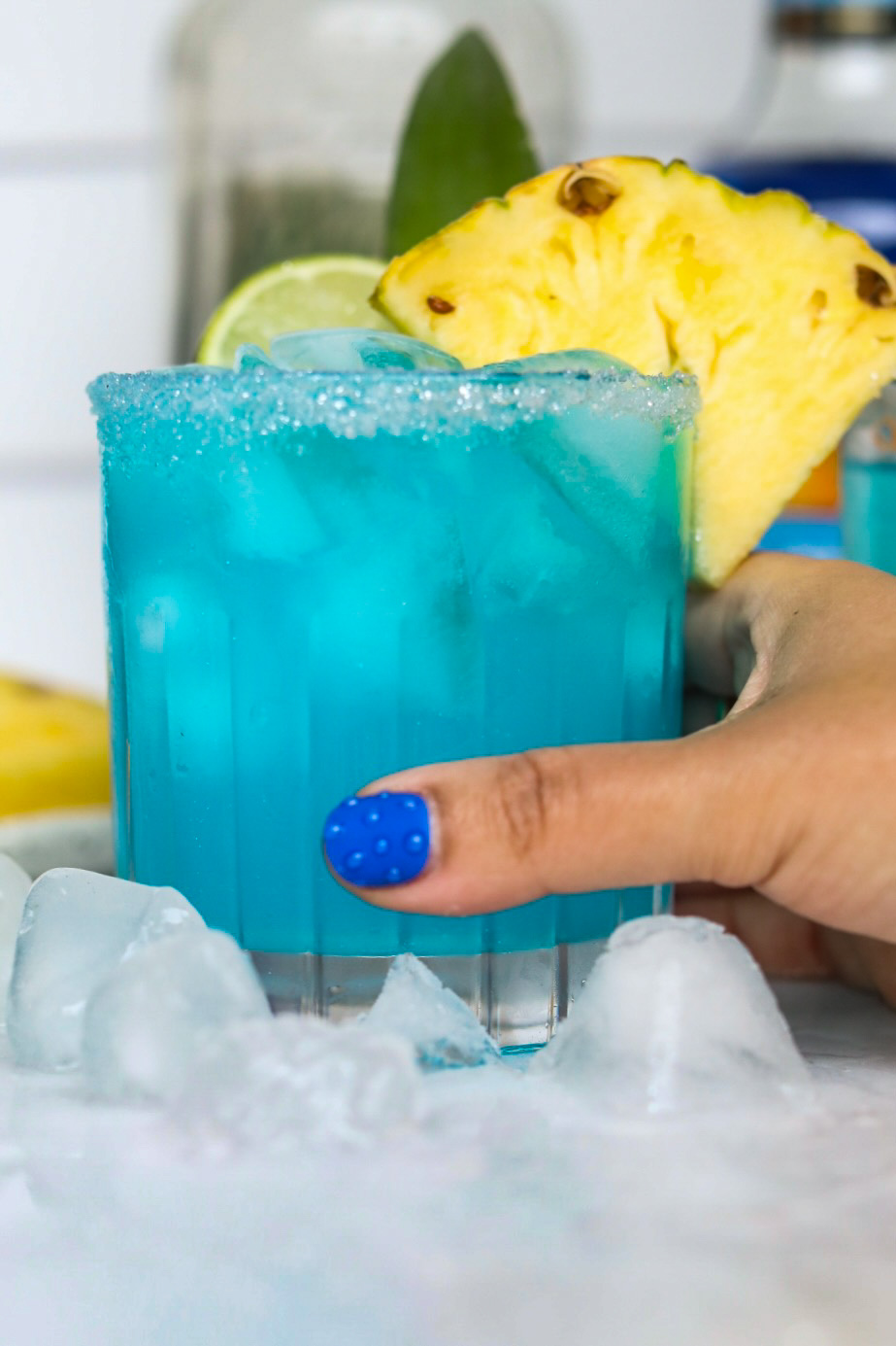 Hand with blue nail on thumb holding blue margarita recipe.