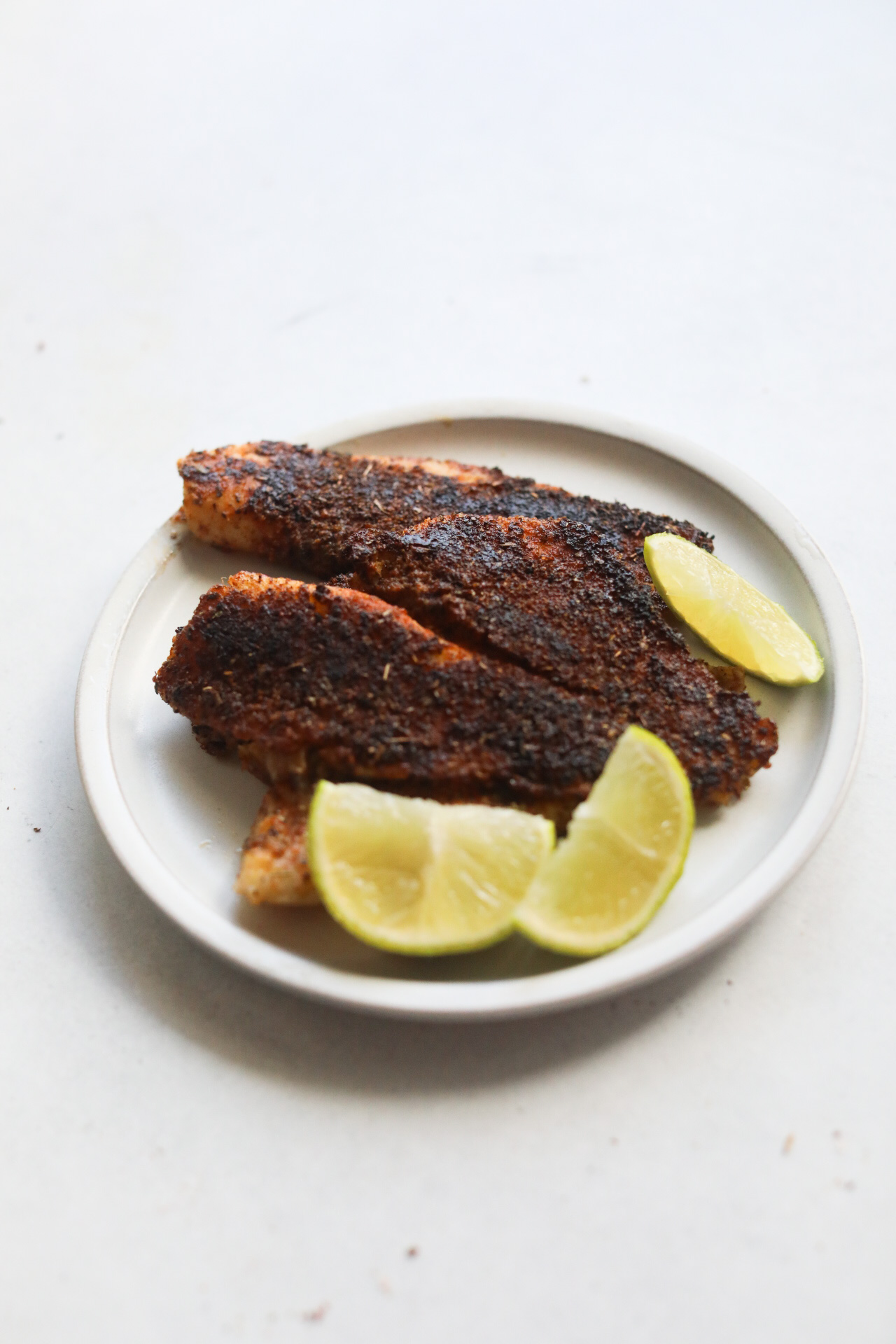 Blackened fish cooked in a small matte plate with sliced limes.