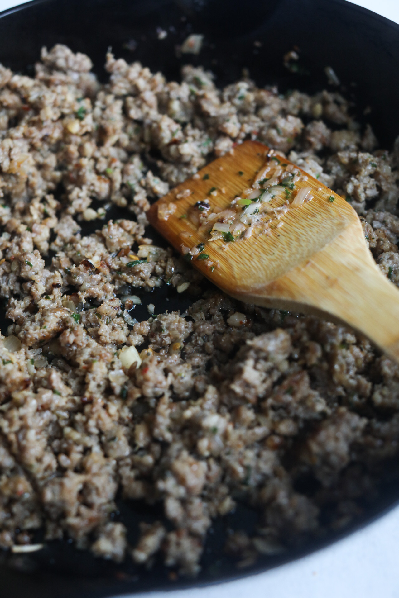 Ground beef and pork mixture browned and cooked in black cast iron skillet with wooden spoon.