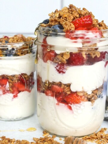 Featured image of Greek Yogurt Parfait with two mason jars filled with yogurt, fresh fruit, granola and honey drizzle.