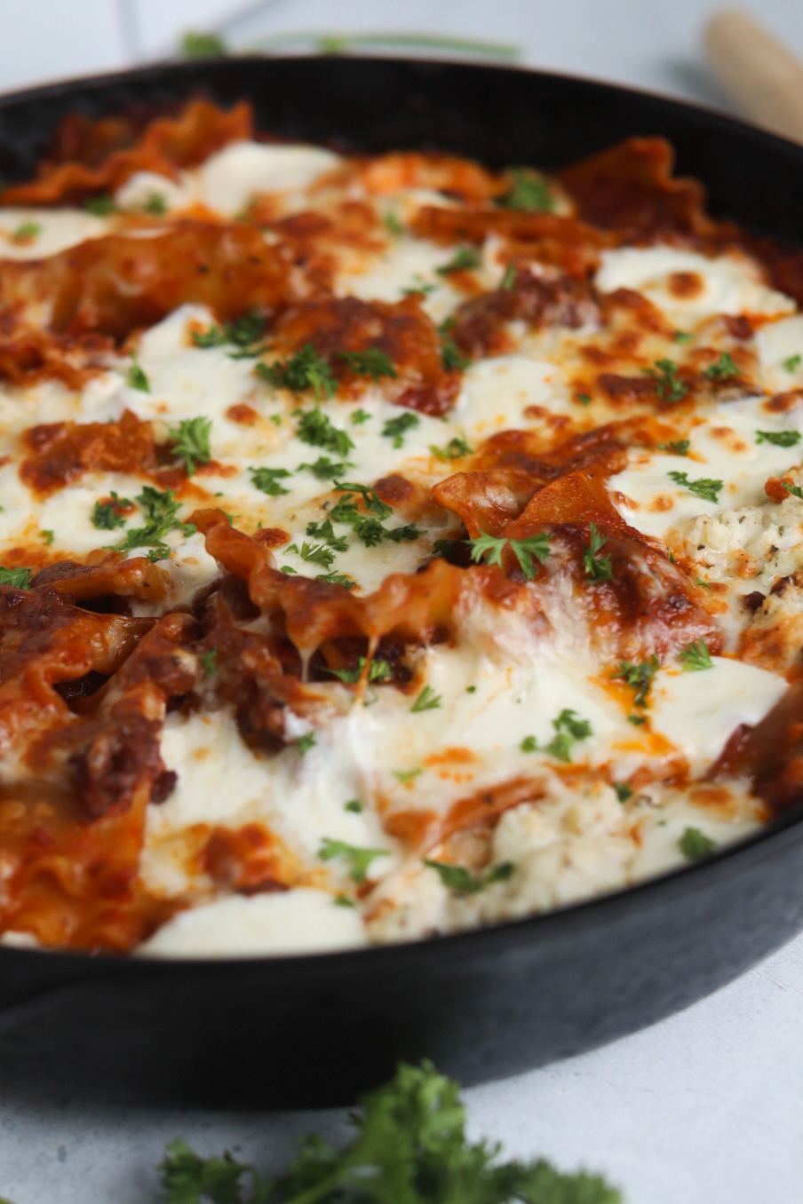 Skillet lasagna in a black cast iron skillet topped with melted mozzarella cheese, topped with fresh parsley.