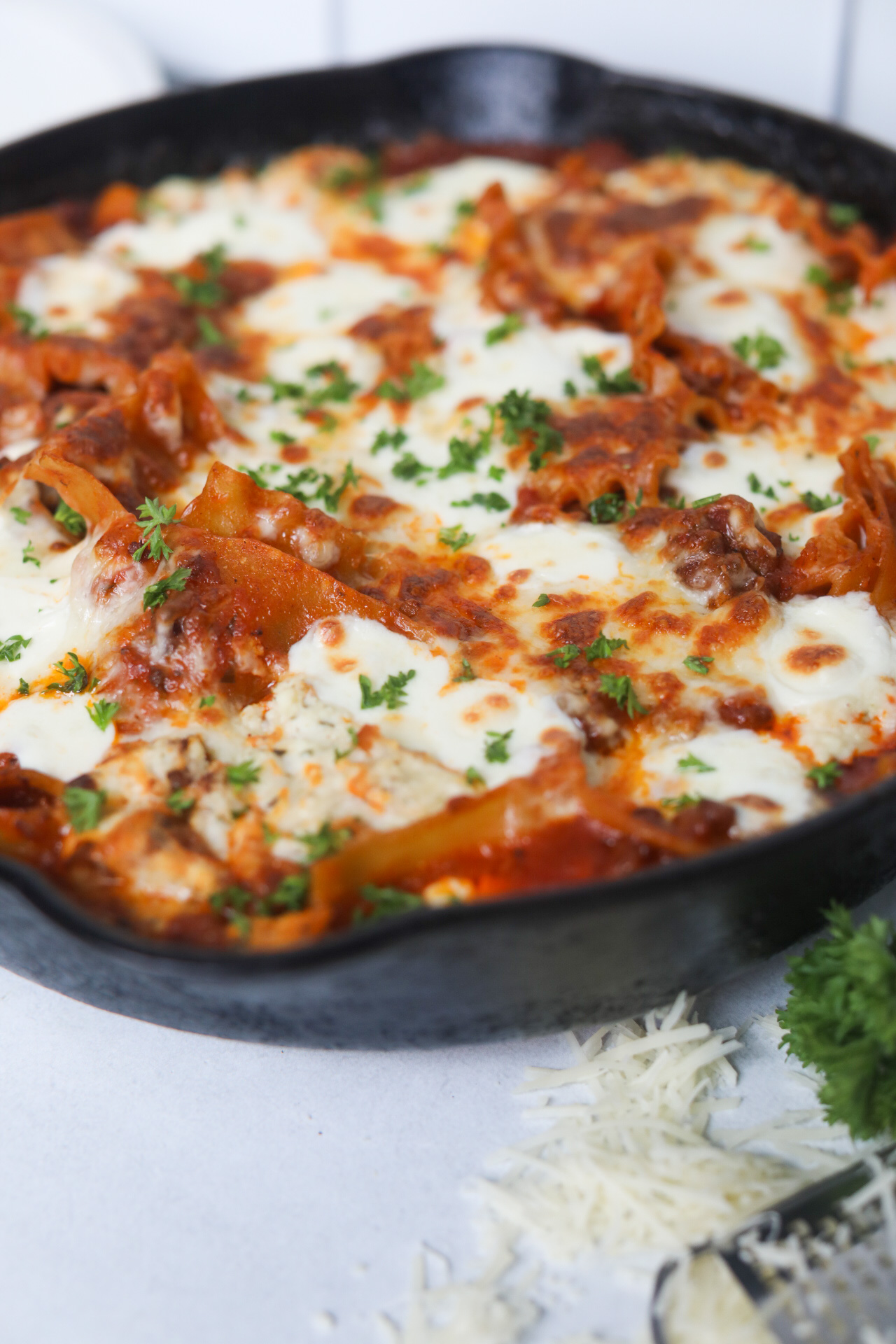 Final imaged of one pot skillet lasagna in a black cast iron skillet. Bunch of parsley and black and white kitchen towel added for styling purposes.