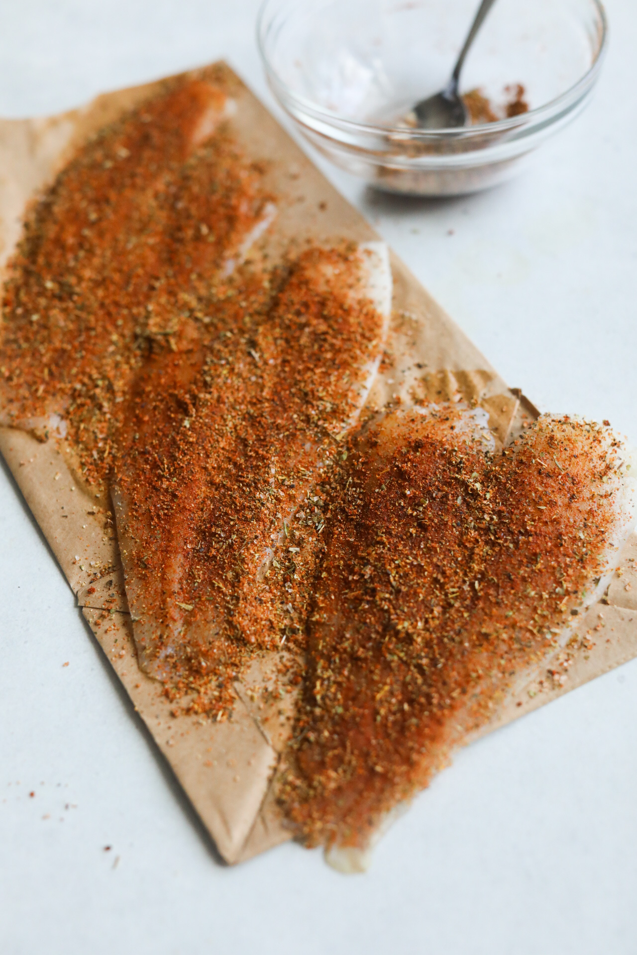 Catfish with blackened seasoning before being cooked on brown paper.