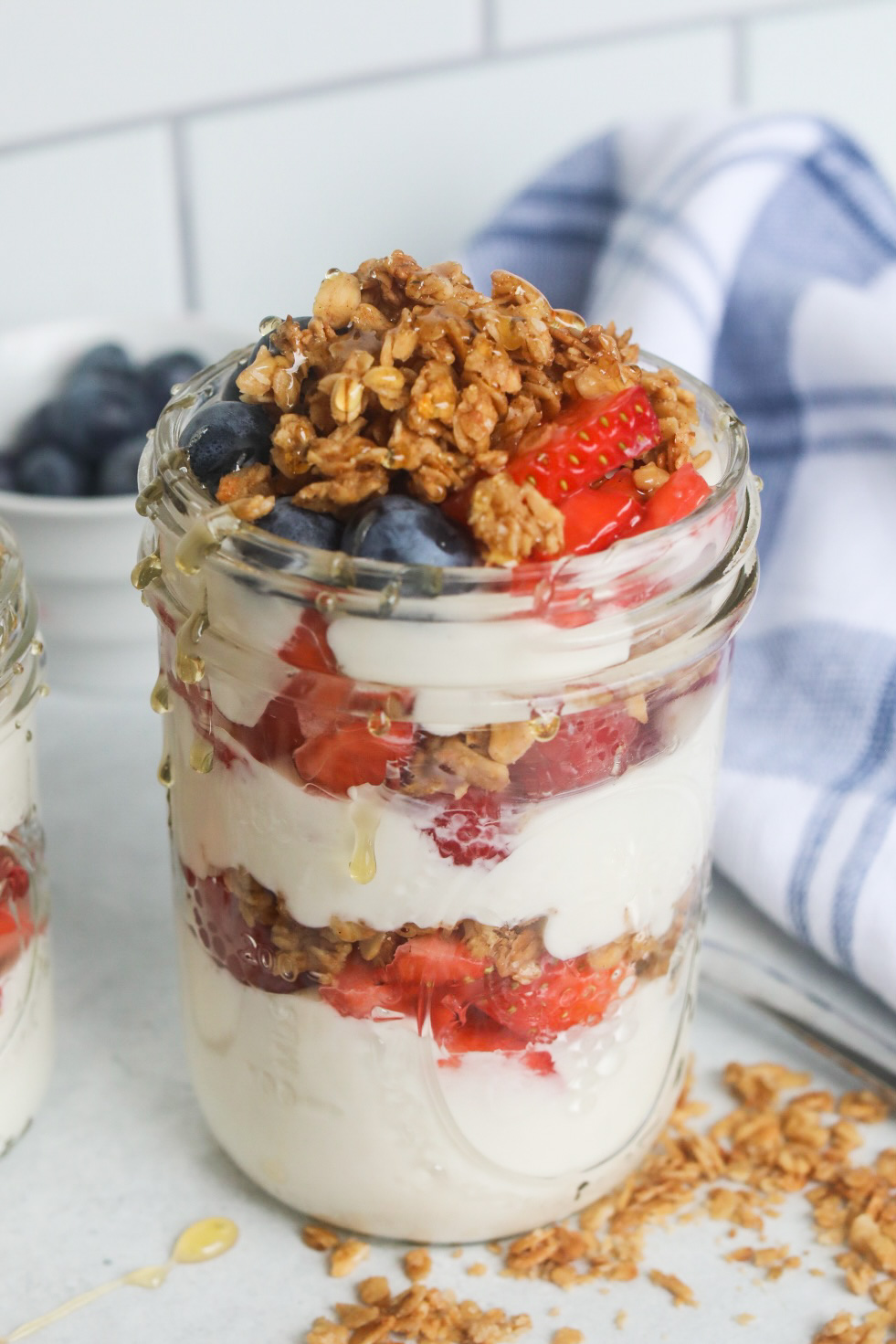 Greek yogurt parfait, plated in a short glass mason jar topped with fresh fruit and granola.