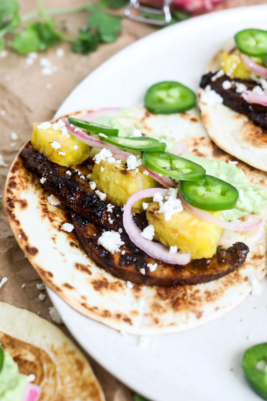 Portobello mushroom tacos plated showing one taco. Grilled mushrooms, pineapple, jalapeño, pickled onion topped with queso crumble.