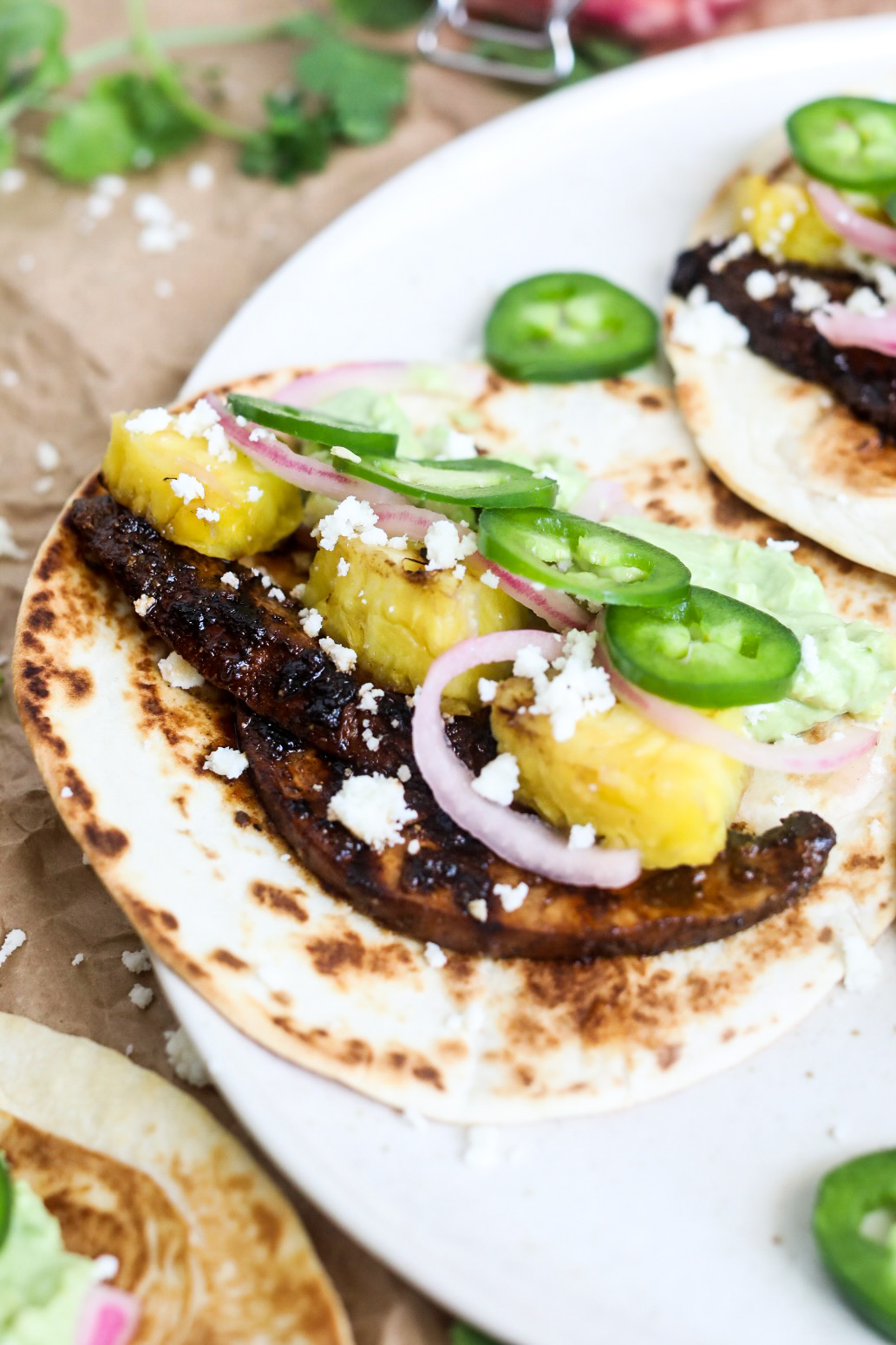 Portobello mushroom tacos plated showing one taco. Grilled mushrooms, pineapple, jalapeño, pickled onion topped with queso crumble. 