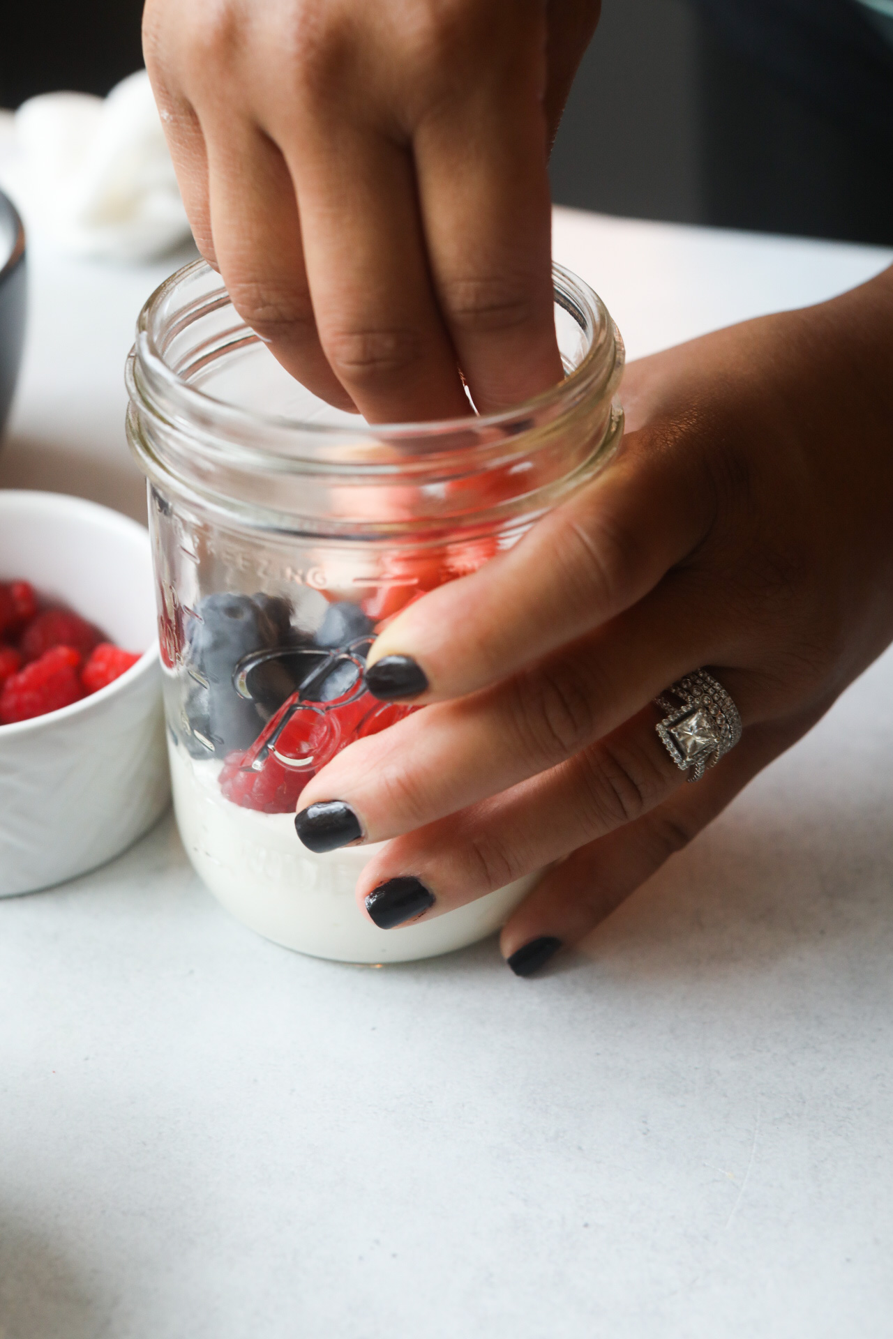 Greek yogurt parfait with hand preparing the yogurt in a mason jar, hand is adding strawberries.