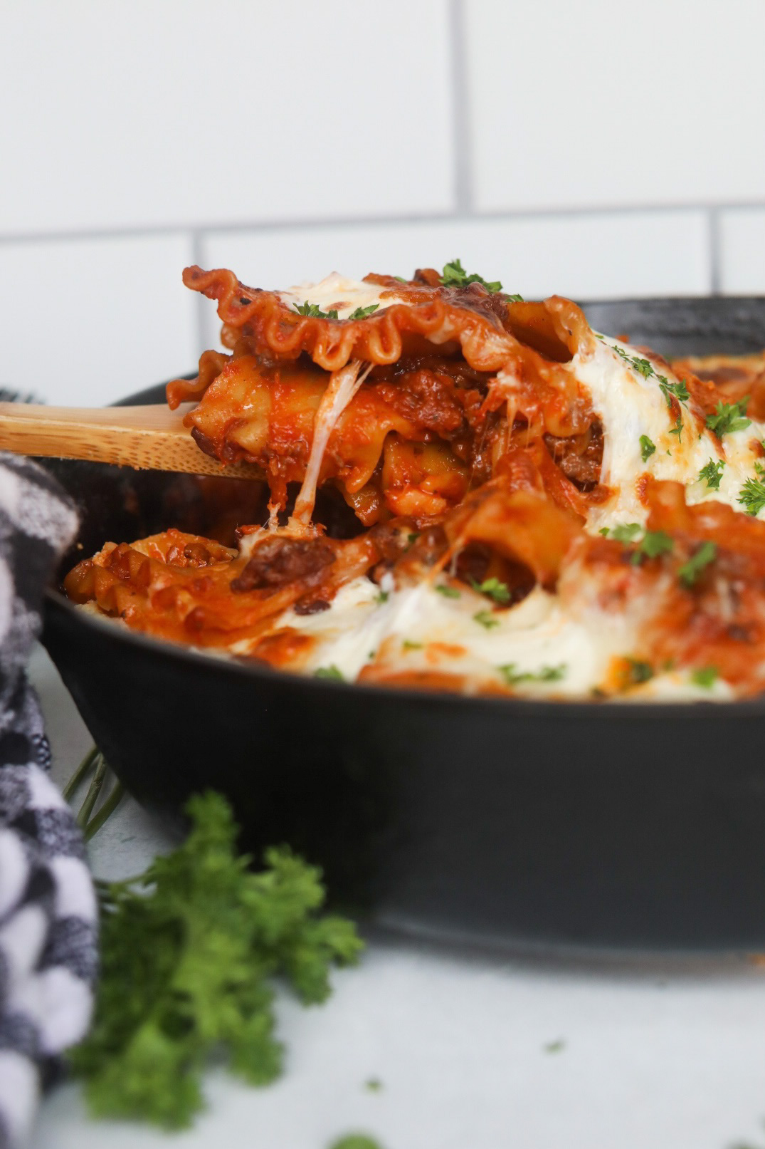 Image of cheese pull image of completed lasagna being scooped out by a wooden spoon.