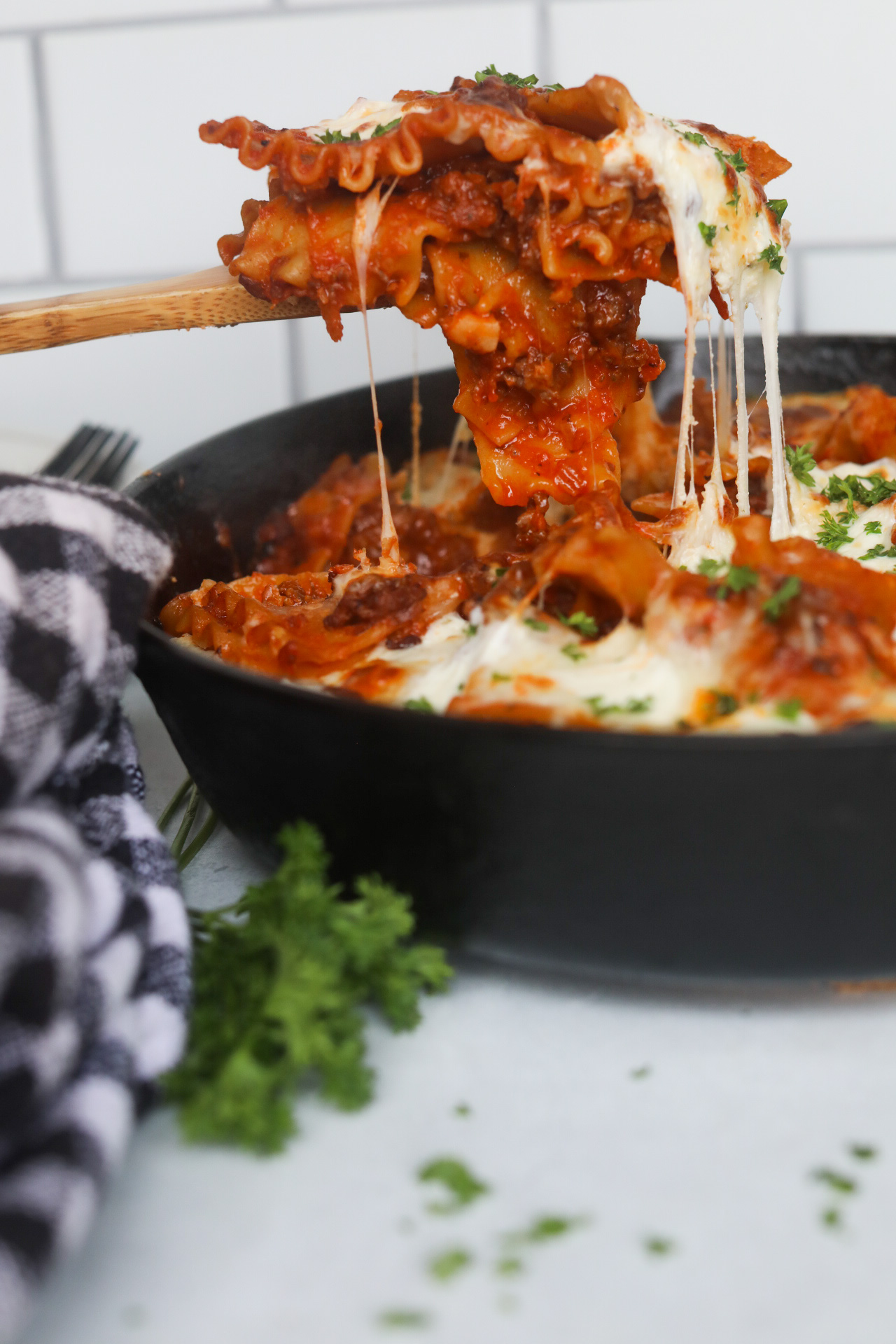 one skillet lasagna Cheese pull image of completed lasagna being scooped out by a wooden spoon.