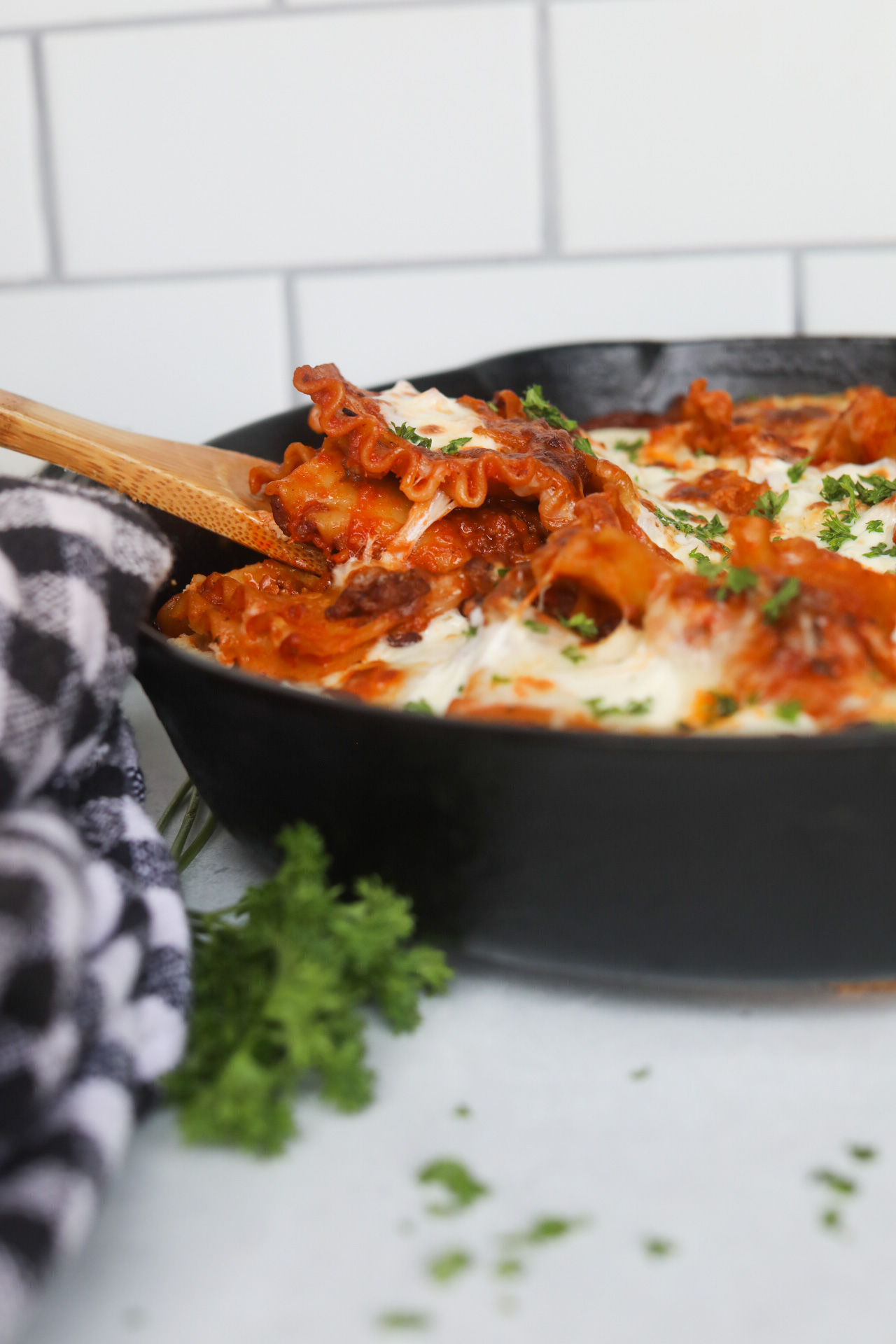 Process image of cheese pull image of completed lasagna being scooped out by a wooden spoon.