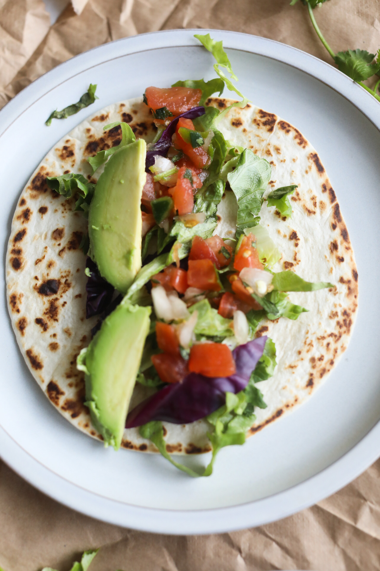 Process shot with tortilla, lettuce, avocado and cabbage on a gray matte plate.