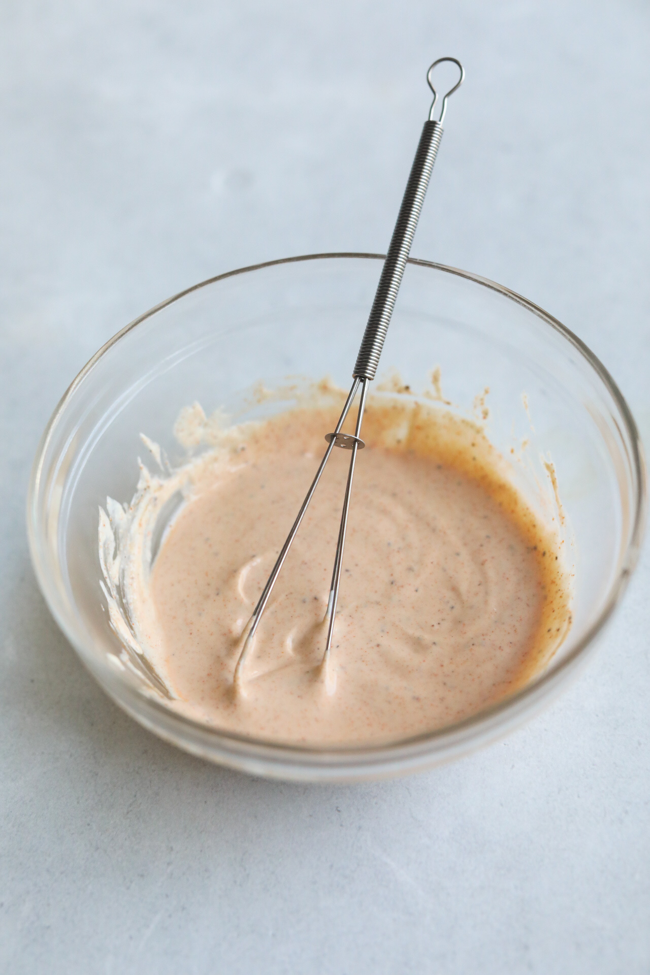 Remoulade sauce ingredients before being whipped and after in clear bowls with a whisk.