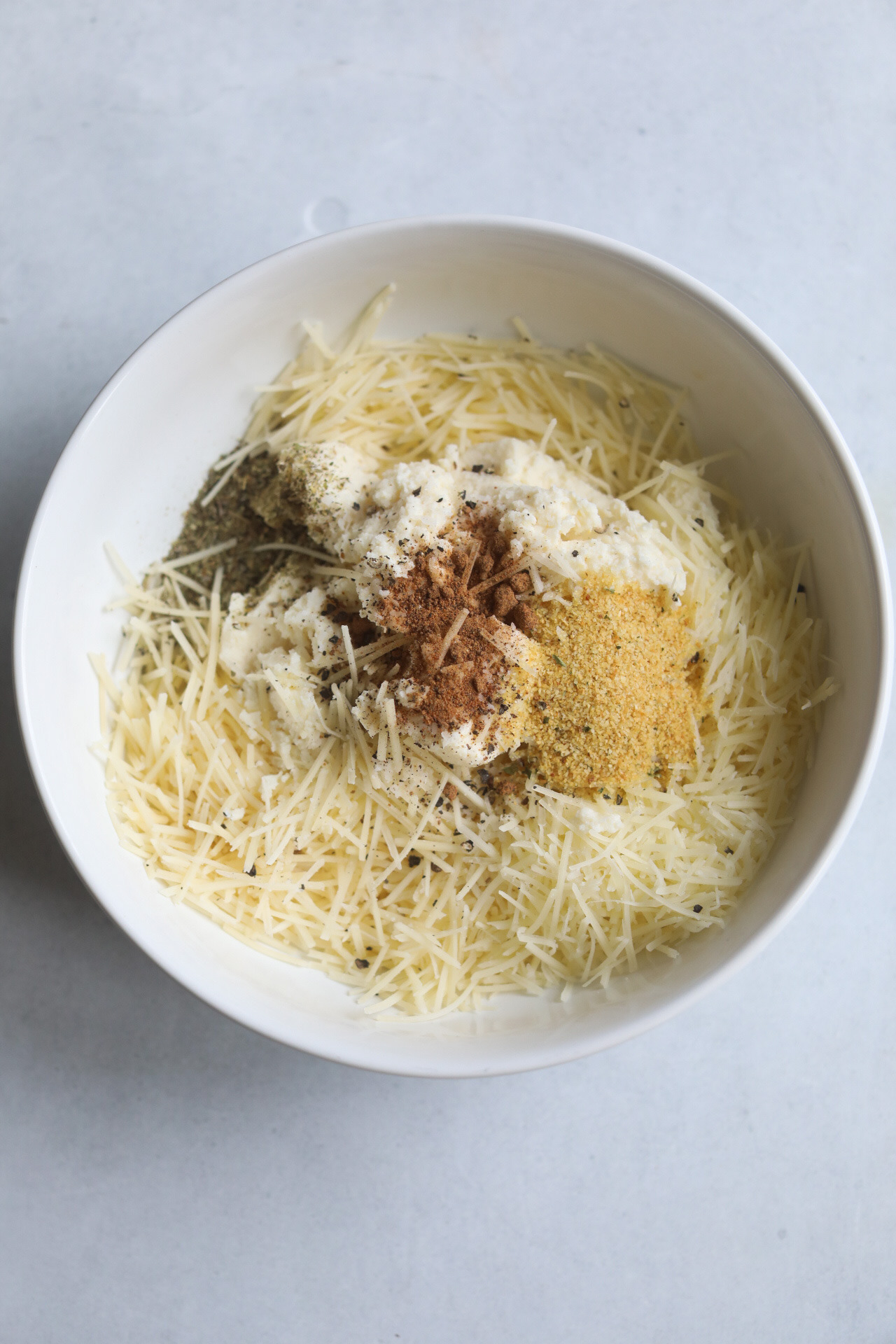 Ricotta mixture in a white bowl with ricotta, asiago cheese and blended seasonings.