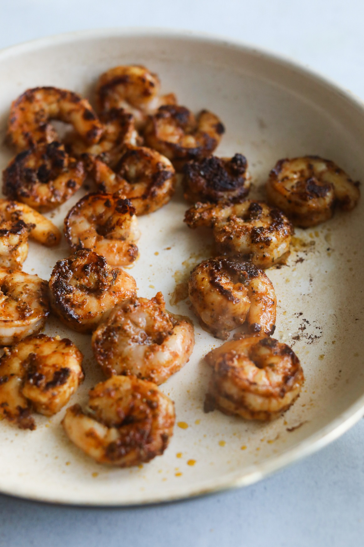 White pan with seasoned shrimp with blackening seasoning.