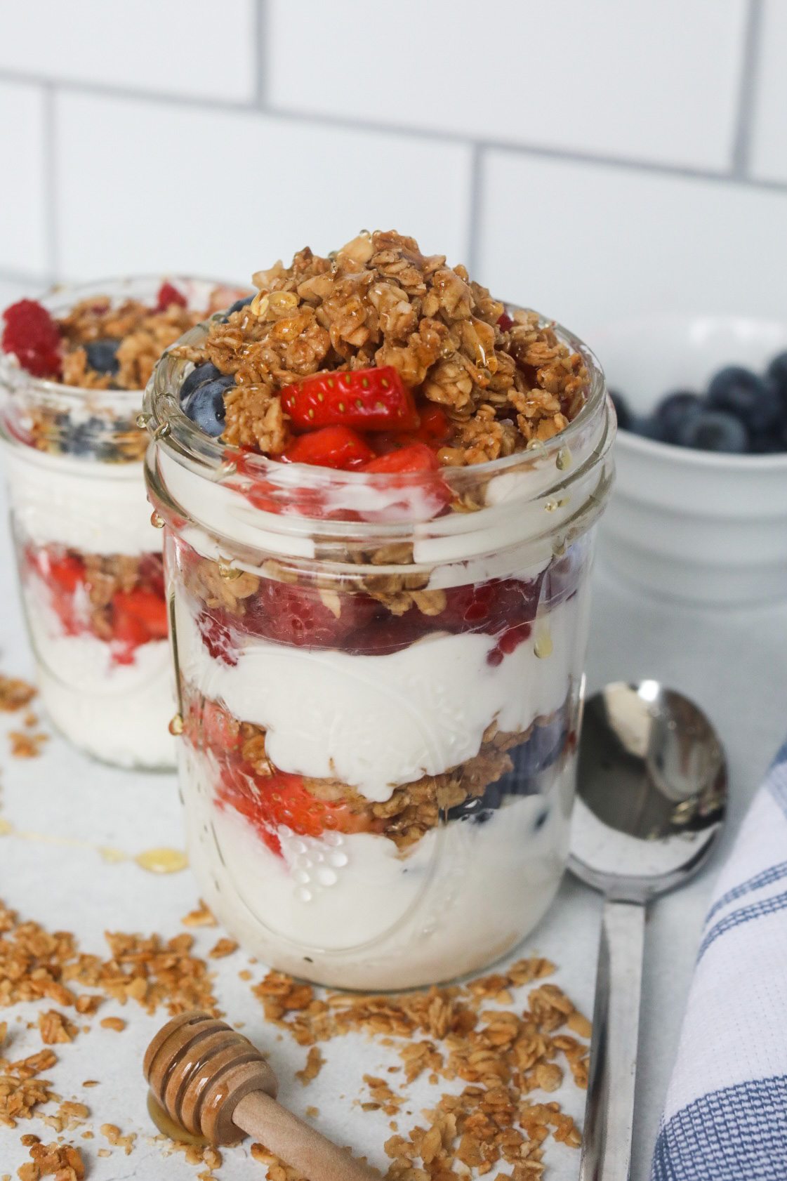 Final image of plated Greek Yogurt Parfait with fresh fruit, granola and honey drizzle. Honey stick, extra granola and spoon added for styling purposes.