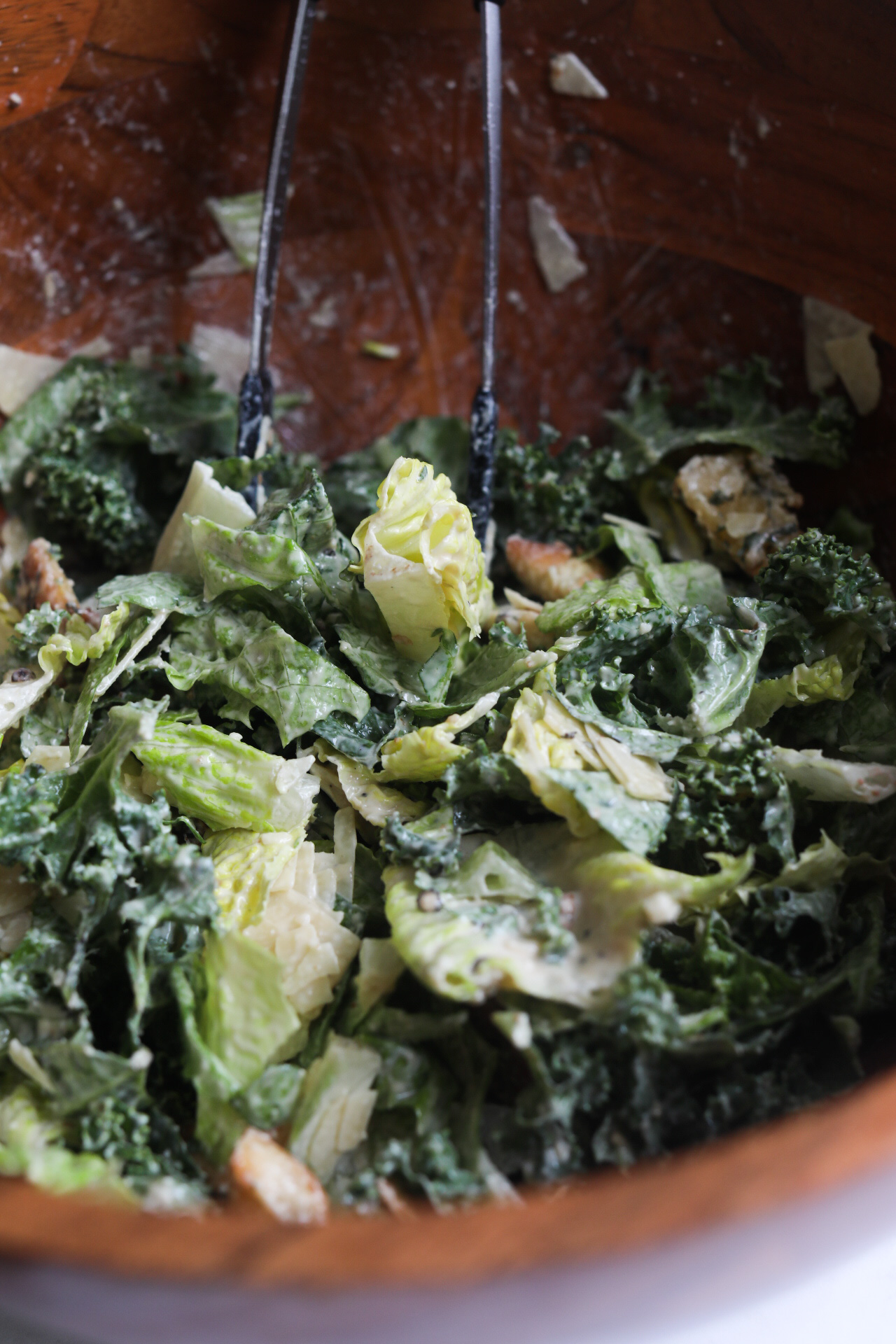 Caesar salad mixed in a wooden bowl with homemade croutons and black tongs.