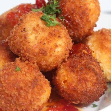 Plated pimento cheese fritters on white plate. Pimento fried balls are piled high, topped with fresh parsley and red pepper sauce.