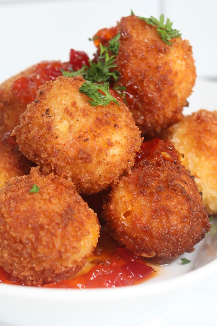 Plated pimento cheese fritters on white plate. Pimento fried balls are piled high, topped with fresh parsley and red pepper sauce.