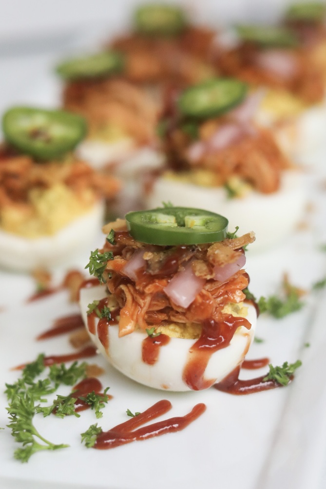 Final recipe shot of loaded bbq chicken deviled eggs. Deviled eggs plated on a white plate and drizzled with bbq sauce.