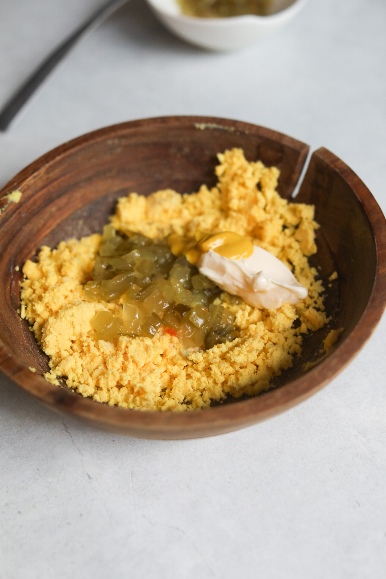 Deviled egg filling in wooden bowl with egg yolks, mayo, mustard, seasoning and relish.