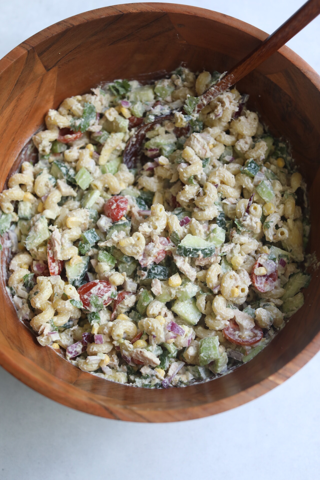 Tuna pasta salad stirred in wooden bowl with wooden spoon. 