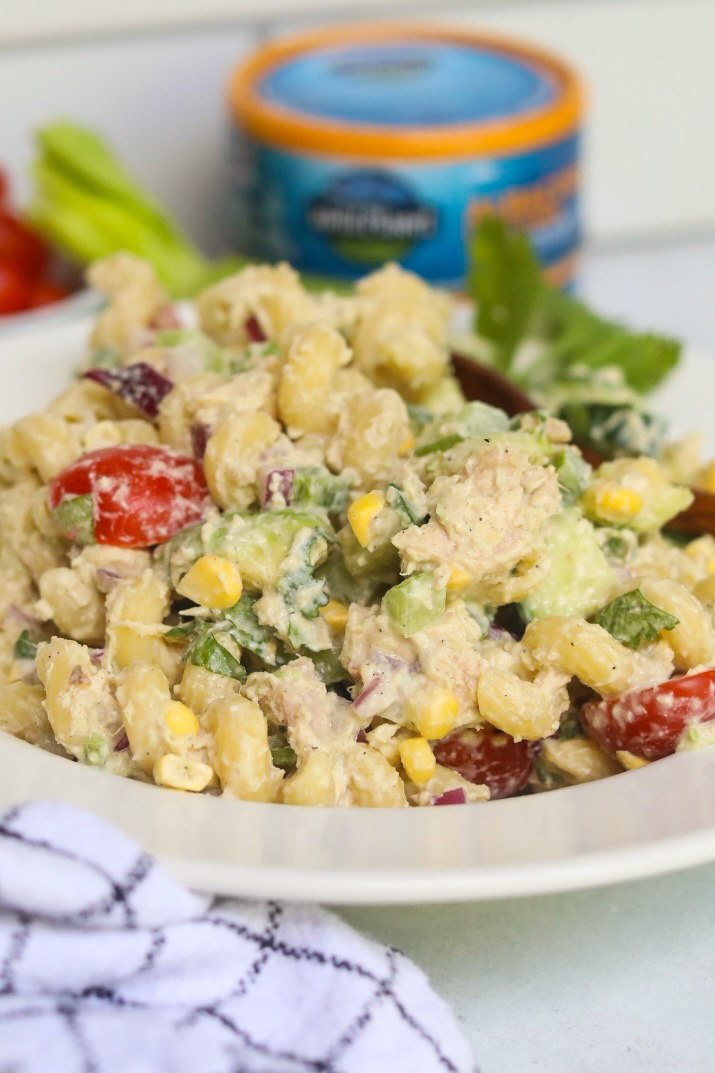 Pasta salad with tuna plated in a white shallow bowl. Fresh herbs, black and white kitchen towel added for styling purposes.