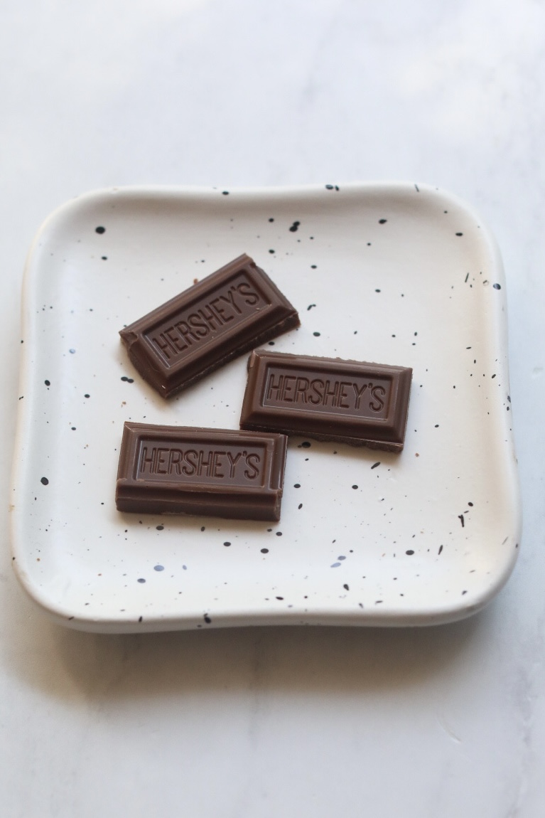 Three small pieces of chocolate on small white plate for sweet chili recipe.