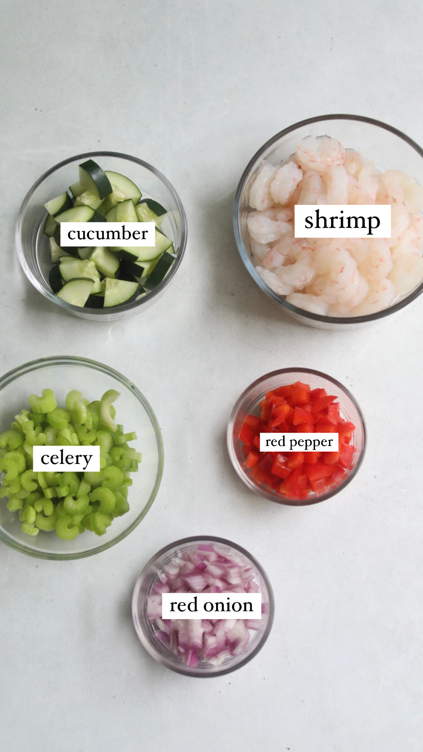 Image of recipe ingredients on a flat lay for shrimp salad recipe. Bowls of red onion, celery, red pepper, cucumber and shrimp.