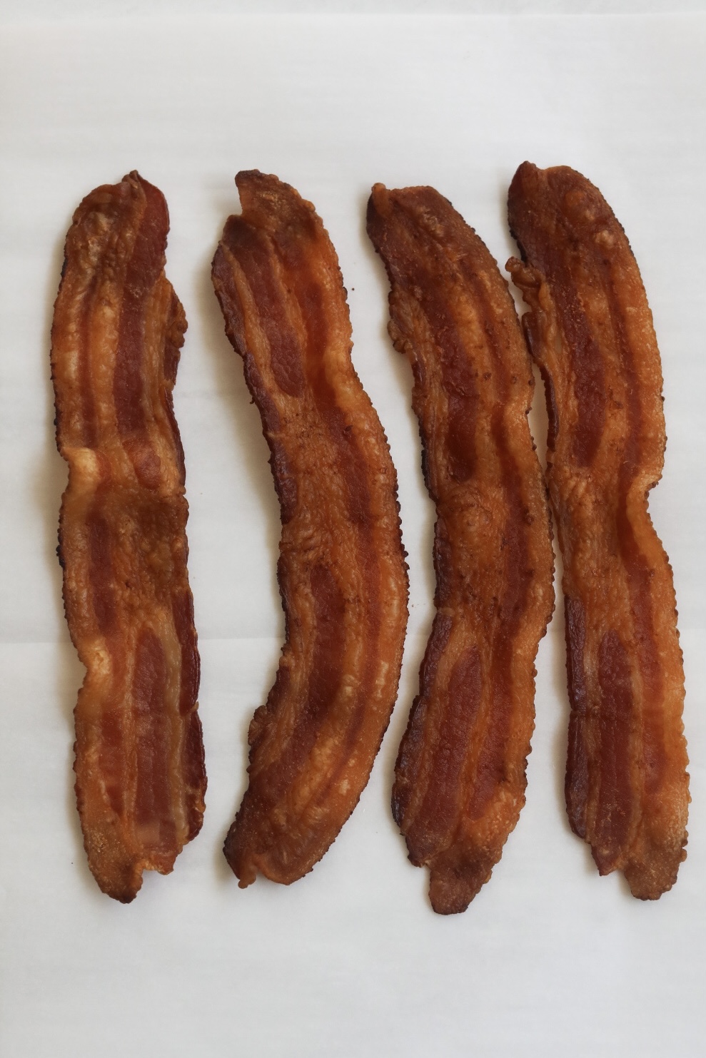 Crispy bacon (4 slices) served on parchment paper for chicken caesar wrap recipe.