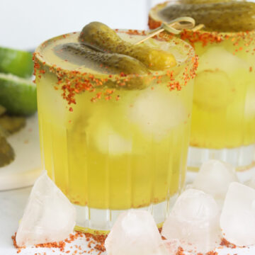 Pickle flavored margarita served in a short glass. Glass is topped with tajin around the rim, filled with ice, topped with a gherkin pickle.