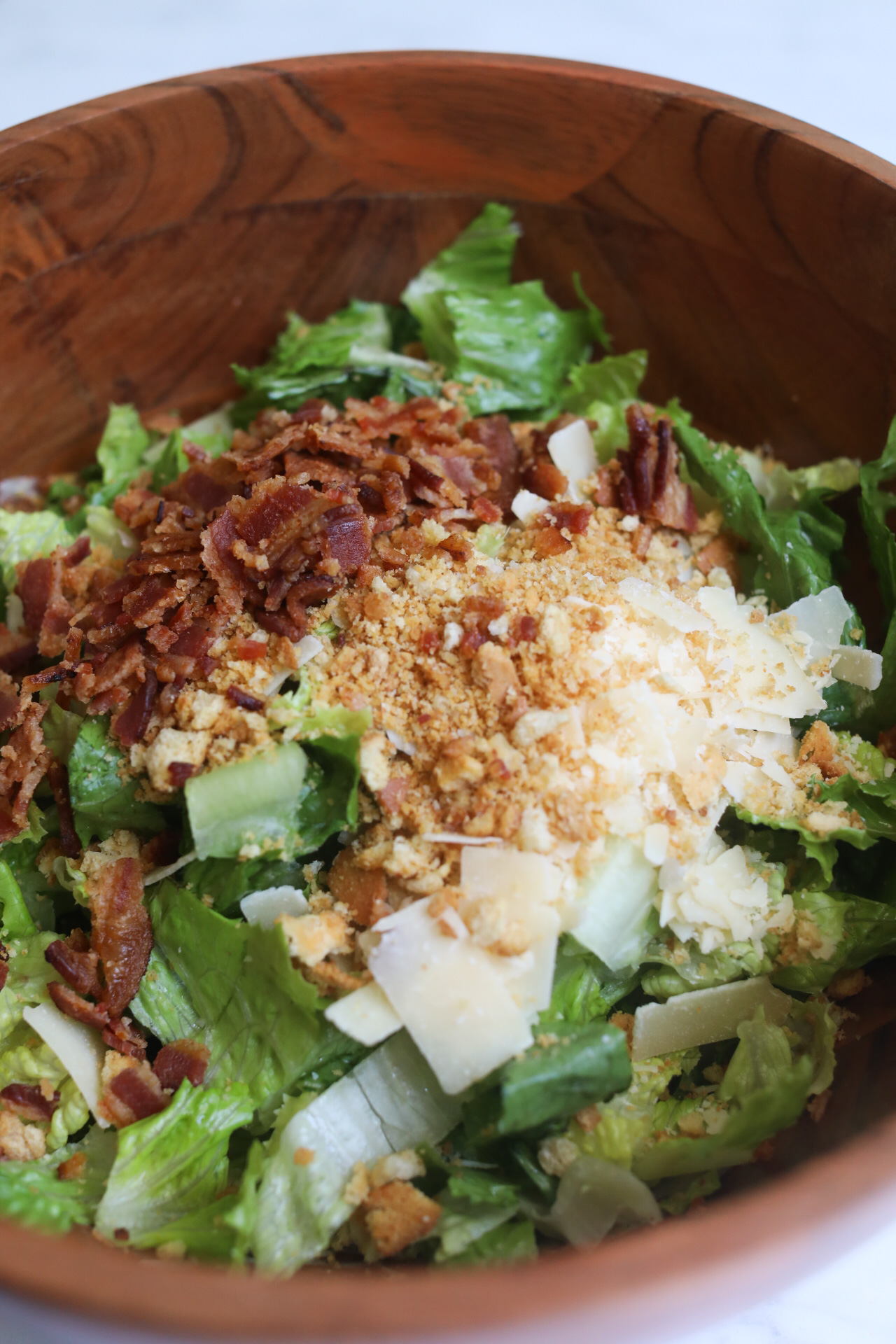 Process shot of caesar salad with romaine lettuce, parmesan cheese and bacon in a large brown wooden bowl.