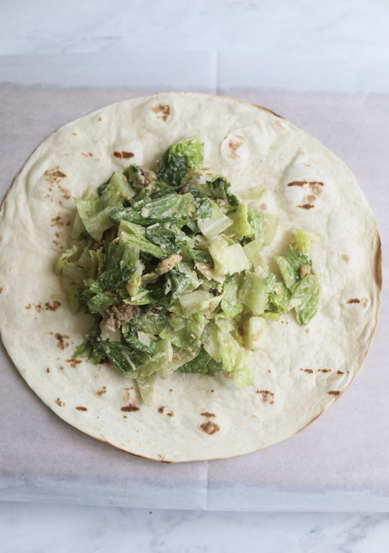 Process shot to show step-by-step process of making Grilled Chicken in a Grill Pan. Large tortilla on top of wax paper with caesar salad.