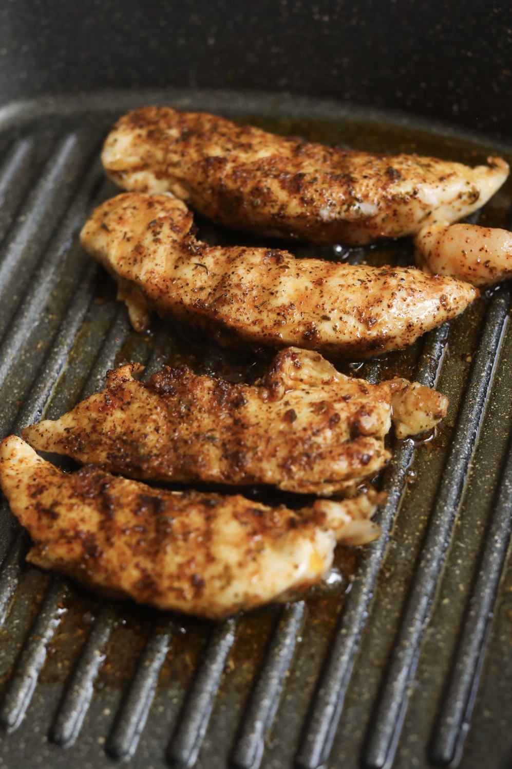 Grilled chicken tenderloins, seasoned, grilling in a grill pan.