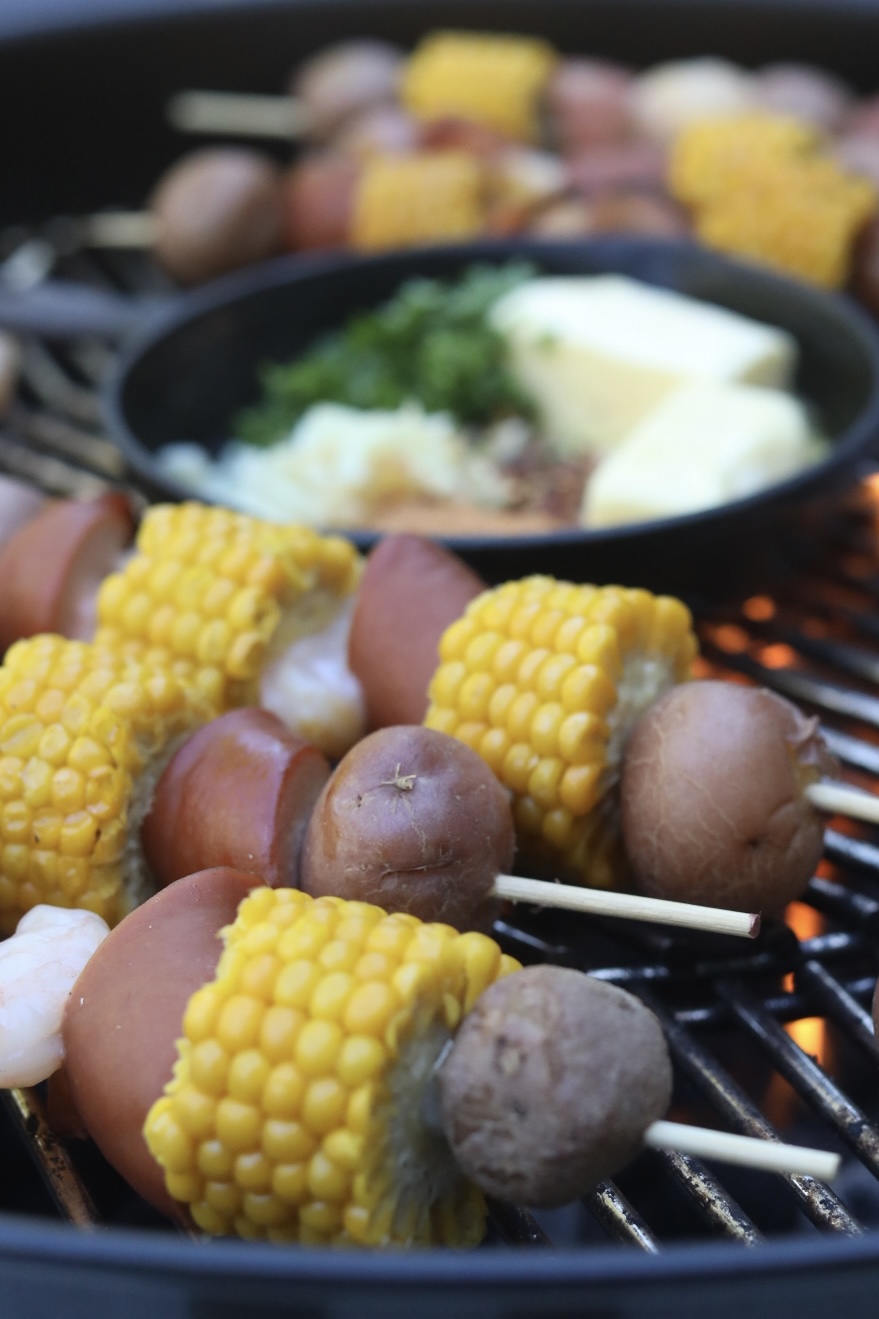 Kabobs are cooking over an open flame on the grill with garlic butter sauce on grill simmering.