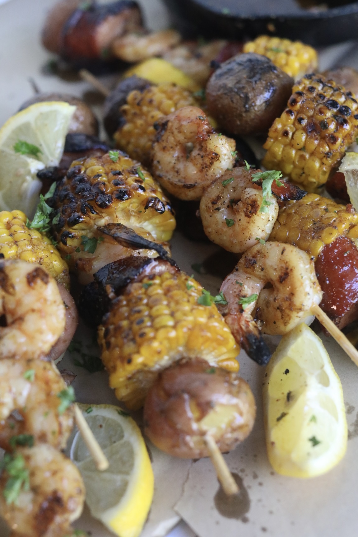 Final recipe images of grilled shrimp kabobs. Kabobs have charred finishes and garnished with fresh lemon slices and parsley.