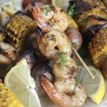 Final recipe images of grilled shrimp kabobs. Shrimp kabobs have charred finishes and garnished with fresh lemon slices and parsley