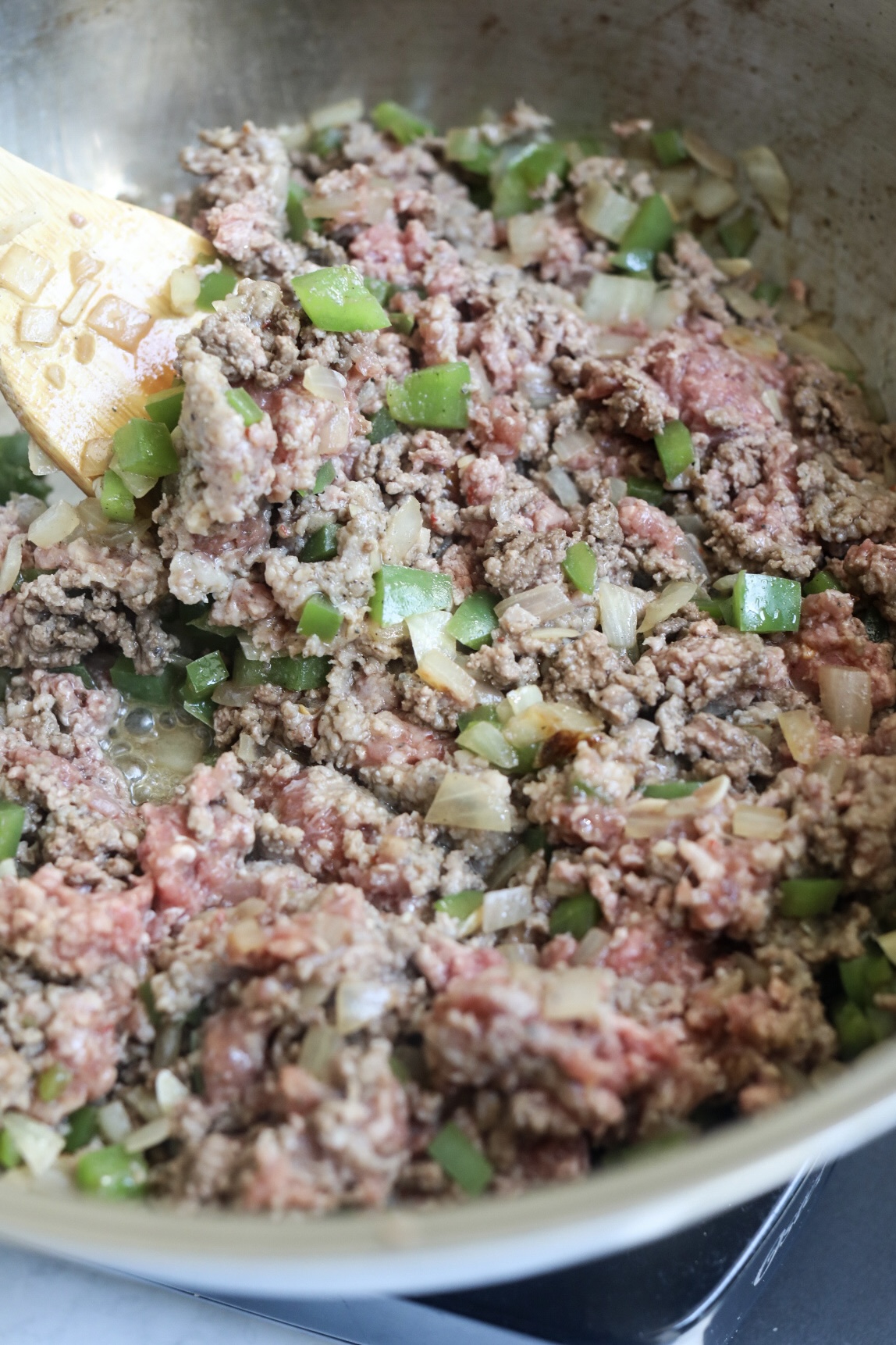 Ground beef and pork mixture with green peppers and onions, sautéing in a pan.