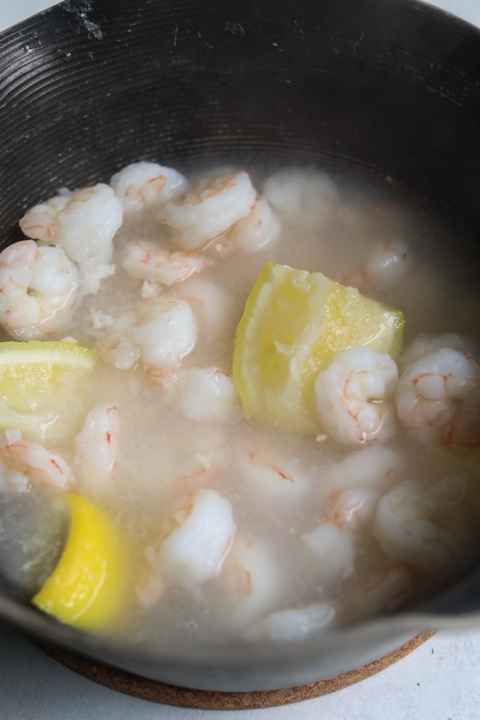 Poached shrimp in a sauce pot cooked with sliced lemons and garlic.