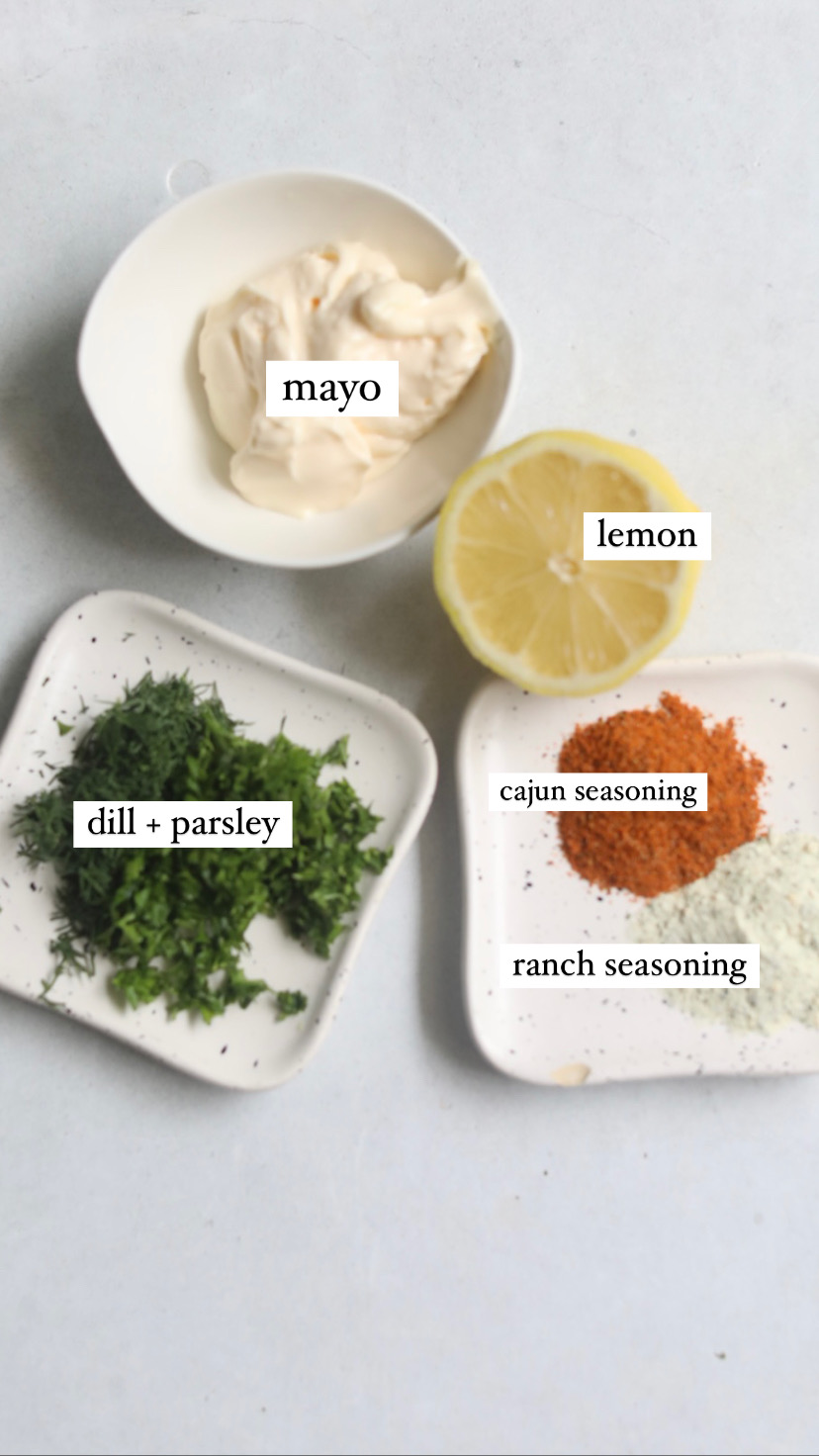 Creamed herb dressing ingredients in a flat lay. Small white bowl of mayo, small flat plates of fresh herbs and seasonings and one half of a lemon.