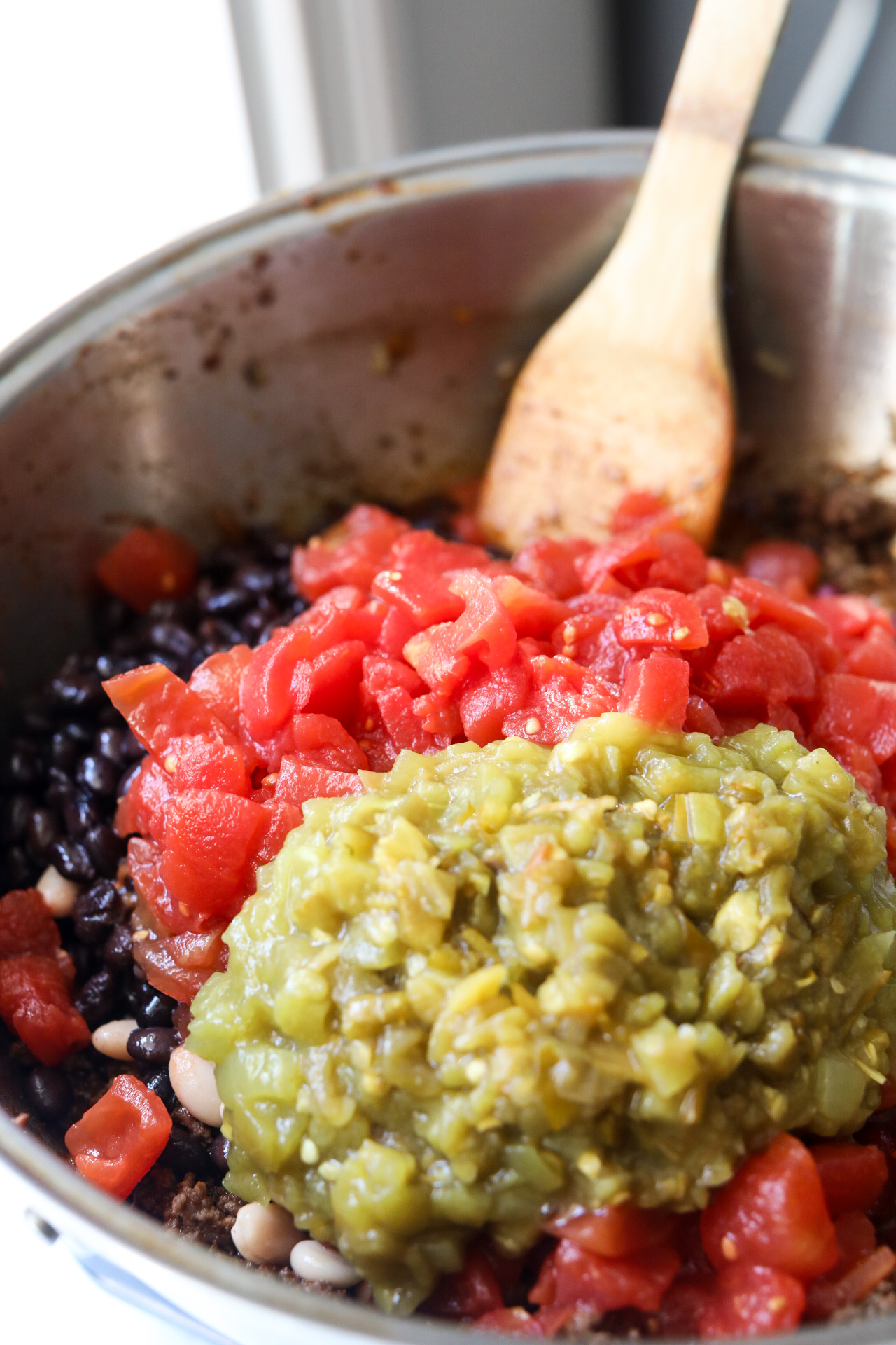 Sweet chili in a large stock pot with beans and diced tomatoes and wooden spoon. 