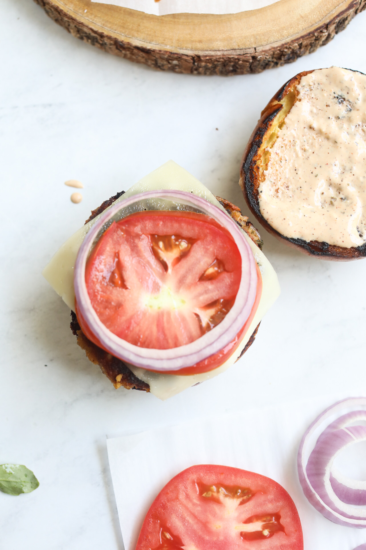 Tuna burger process shot with buns and remoulade sauce, tuna patty with havarti cheese, sliced tomato and sliced red onion.