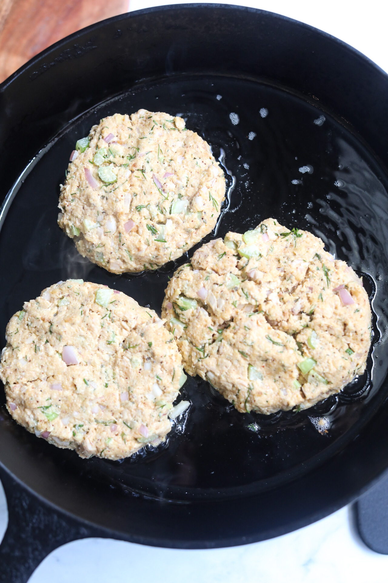 Tuna patties frying in oil in a black cast iron skillet.