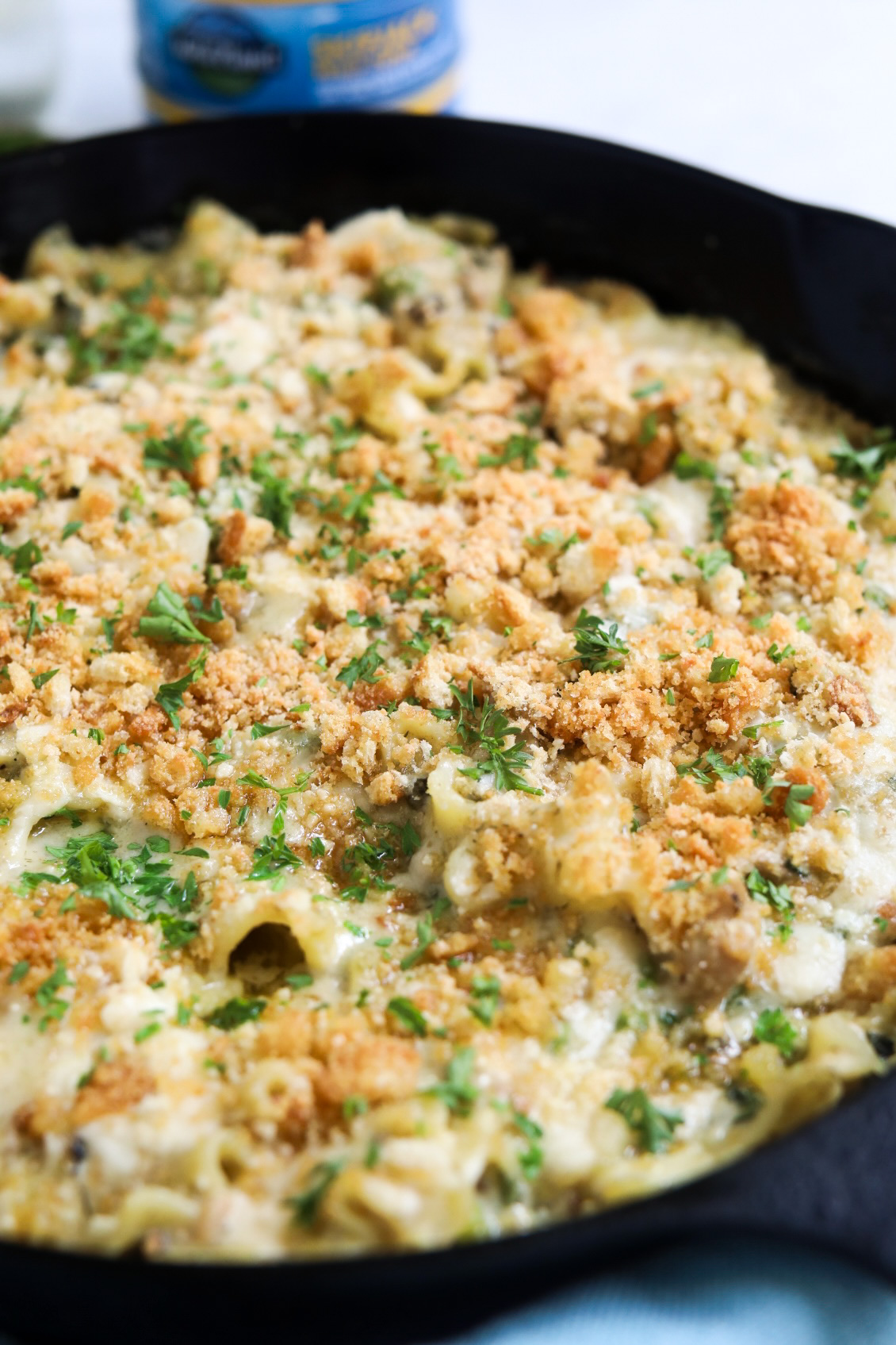 Tuna casserole served in a black cast iron skillet, topped with breadcrumbs and fresh parsley for styling purposes. 