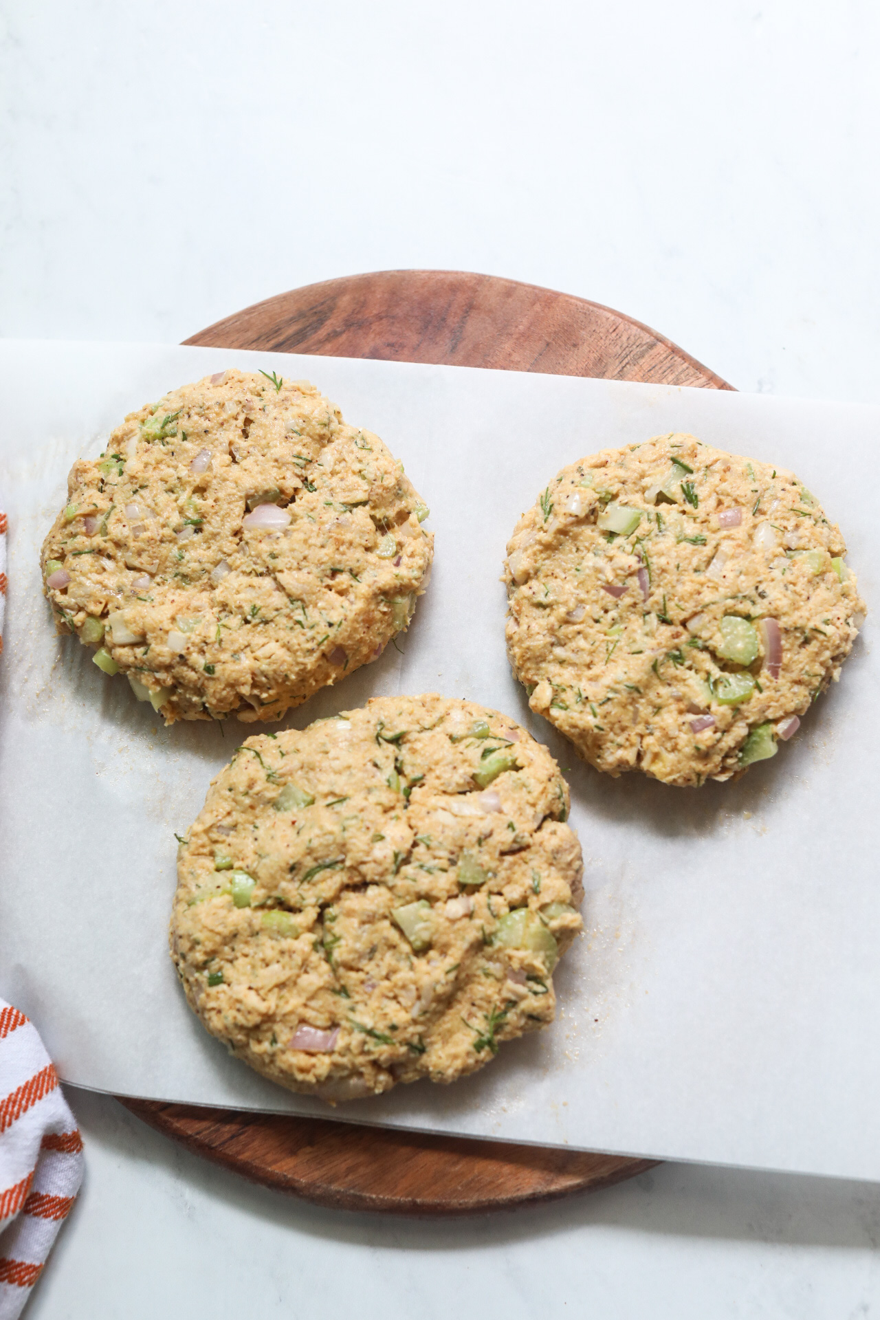Tuna burgers formed into three patties, on a lined cutting board with orange and white towel added for styling purposes.