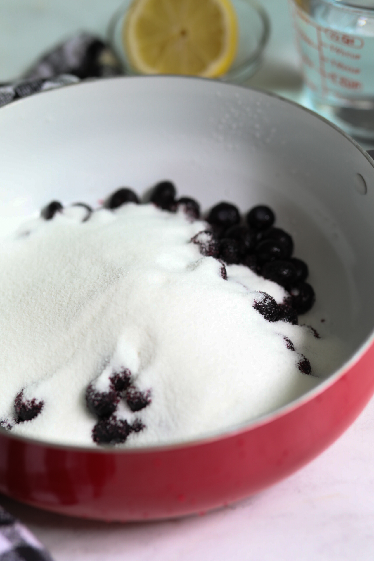 Frozen blueberries with sugar on top to show process of adding ingredients into pot for simmering.