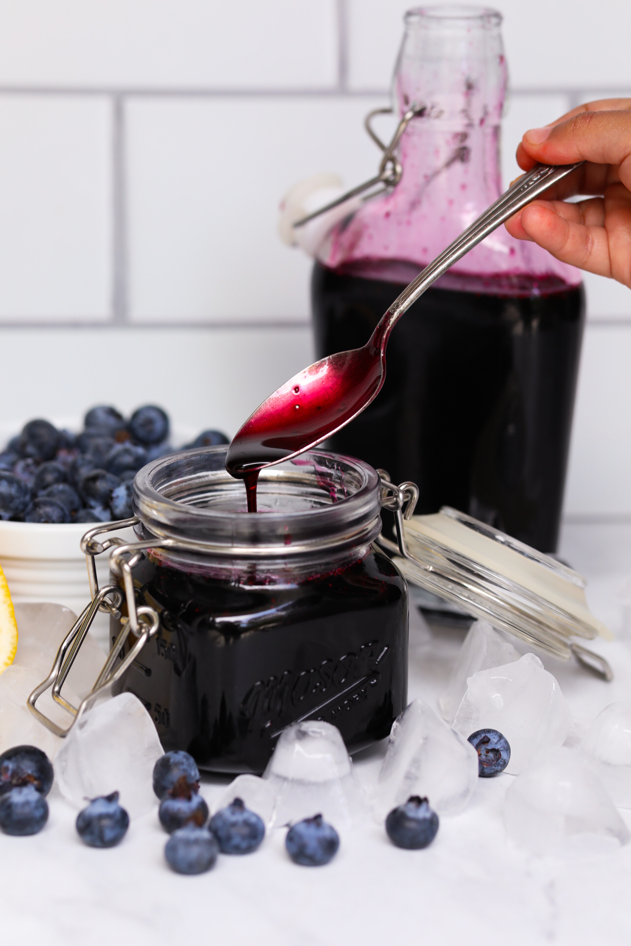 Small hand holding spoon, dipping out blueberry simple syrup to show thickness of sauce.