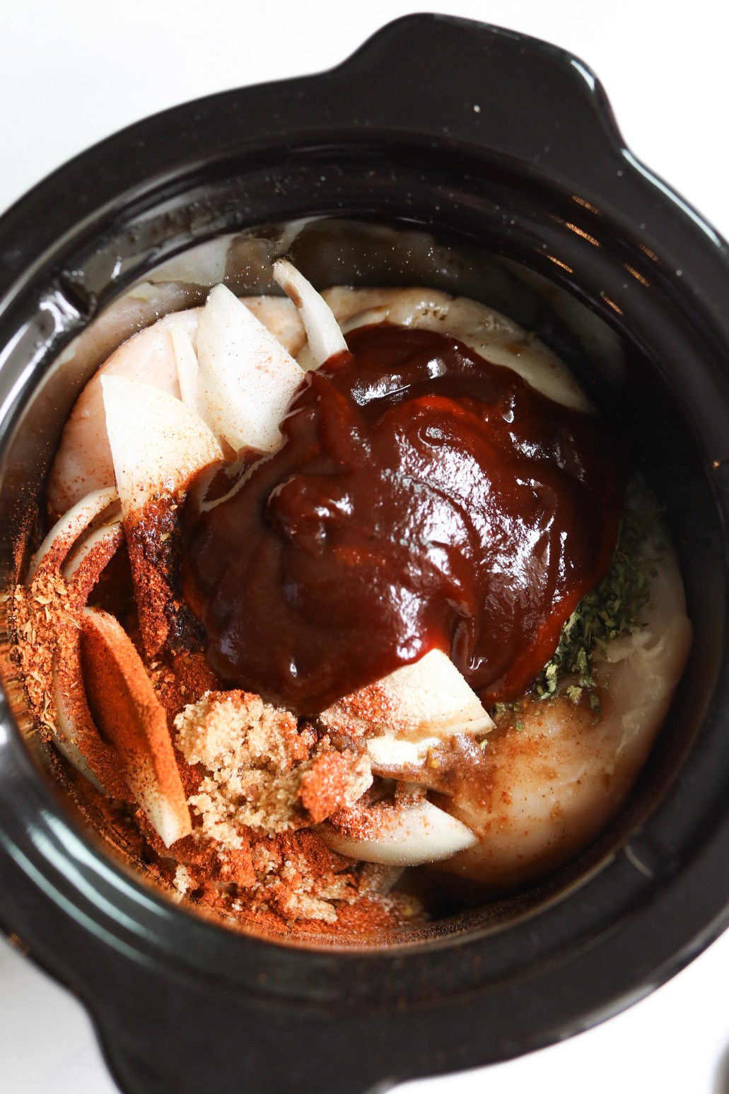 onions, seasoning, and sauce added to a crockpot with chicken